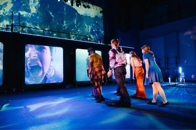 Actors on a stage surrounded by projected images